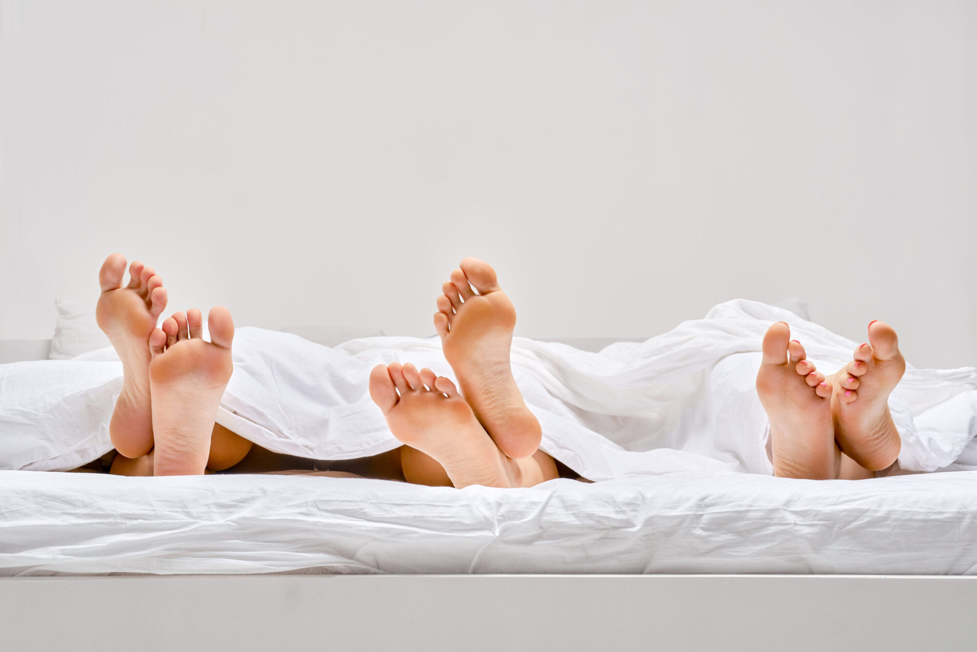 Three pairs of female soles sticking out from under the blanket